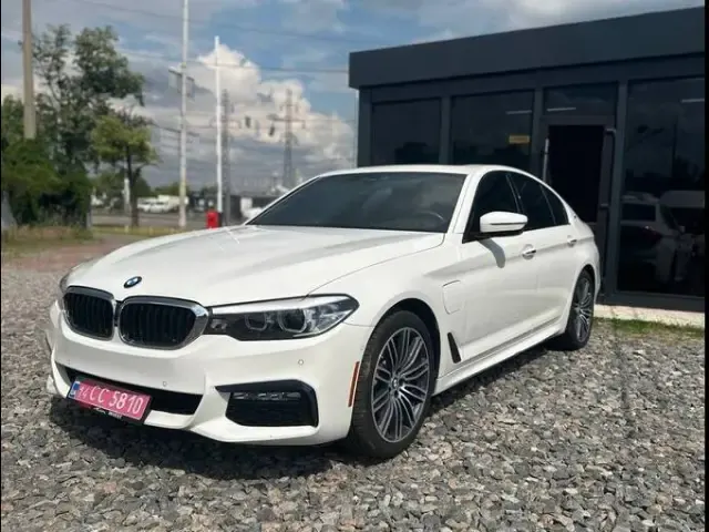 White BMW 5 Series on a gravel lot by a black pavilion