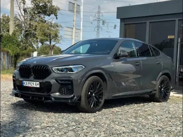 Grey BMW X6 on a gravel lot by a black pavilion