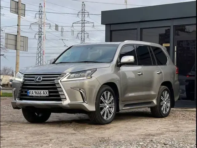 Champagne Lexus LX on a gravel lot, power line pylons behind