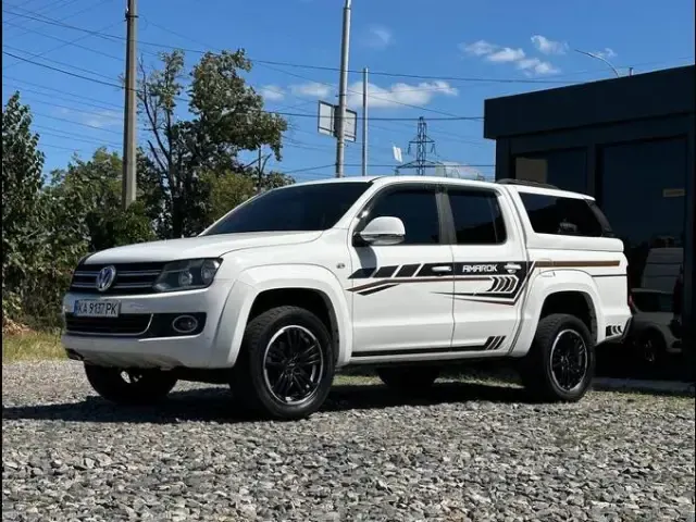 Білий Volkswagen Amarok на гравійному майданчику біля чорного павільйону
